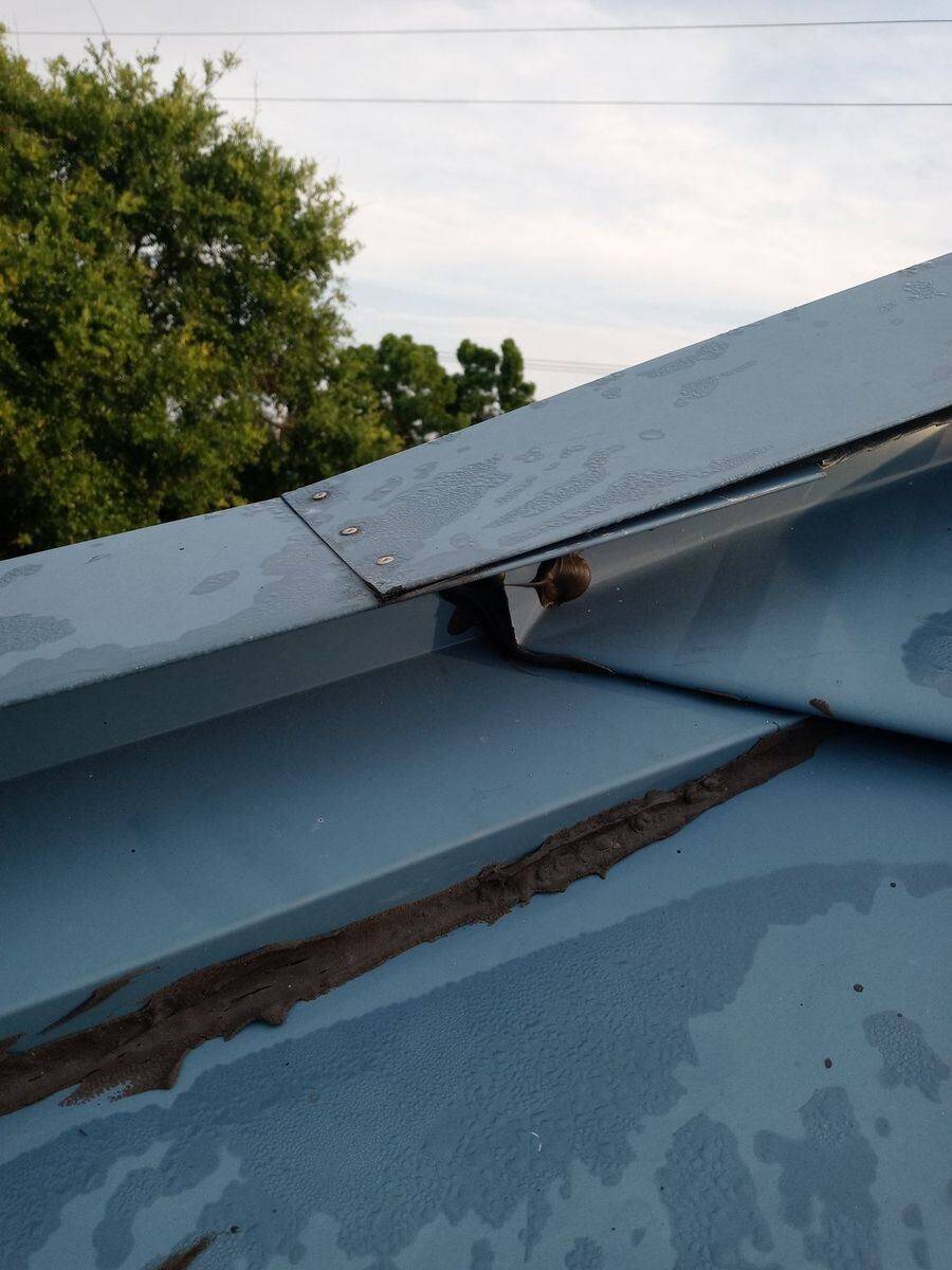 Close-up of an aging metal roof ridge cap with failed, cracked sealant along the panel seam — the kind of roof-condition detail a Florida insurance underwriter flags