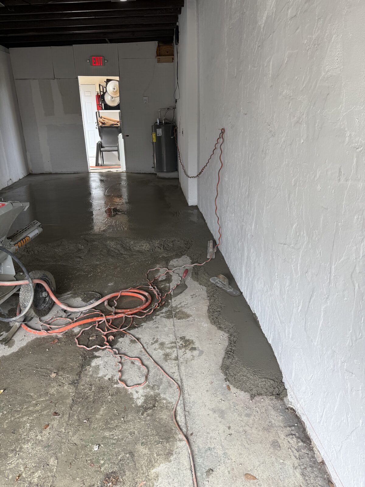Wet floated concrete meeting the remaining bare slab at a clean working edge, air hose and cords run out of the way along the wall