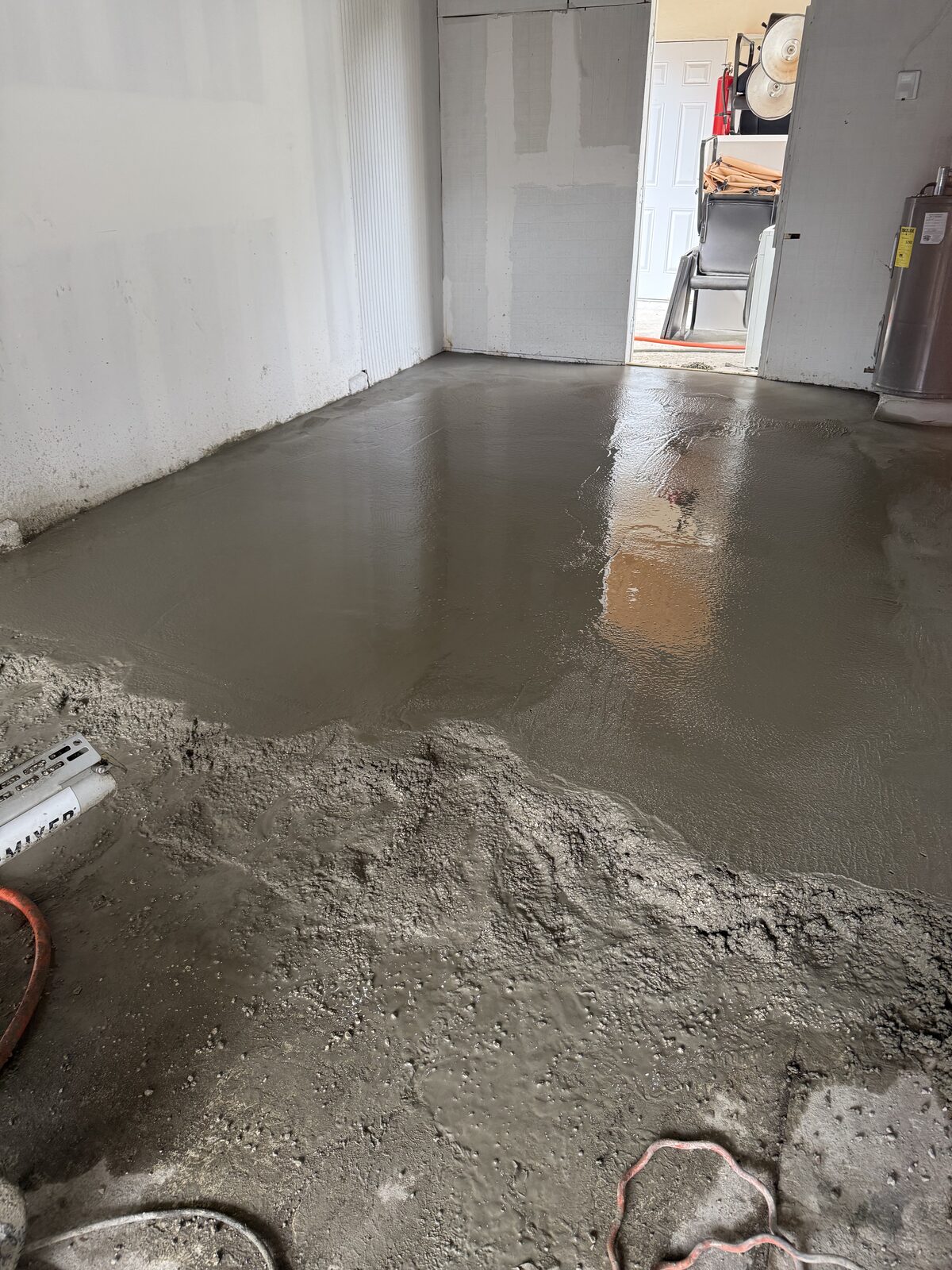 Fresh concrete spread in mounds across the old garage slab, part of the floor already screeded smooth toward the interior doorway