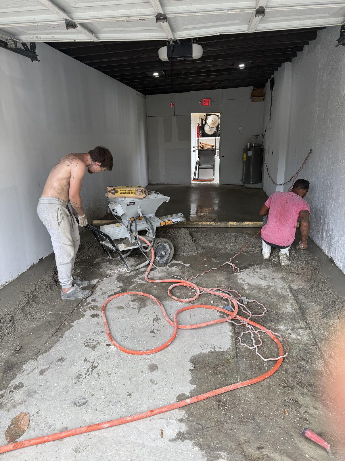 Two crew members placing concrete from a portable mixer inside the garage, one working the mix out toward the wall