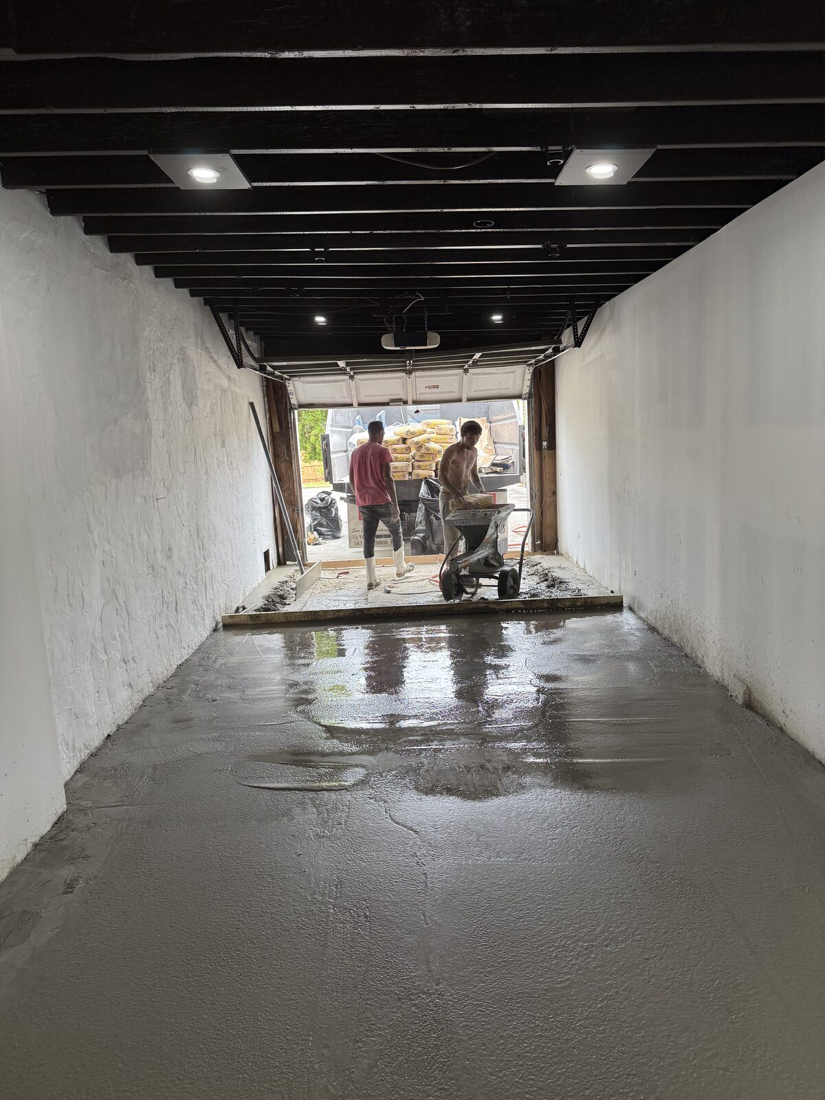 Finished wet concrete floor running level from the rear wall to the door threshold under new recessed ceiling lights