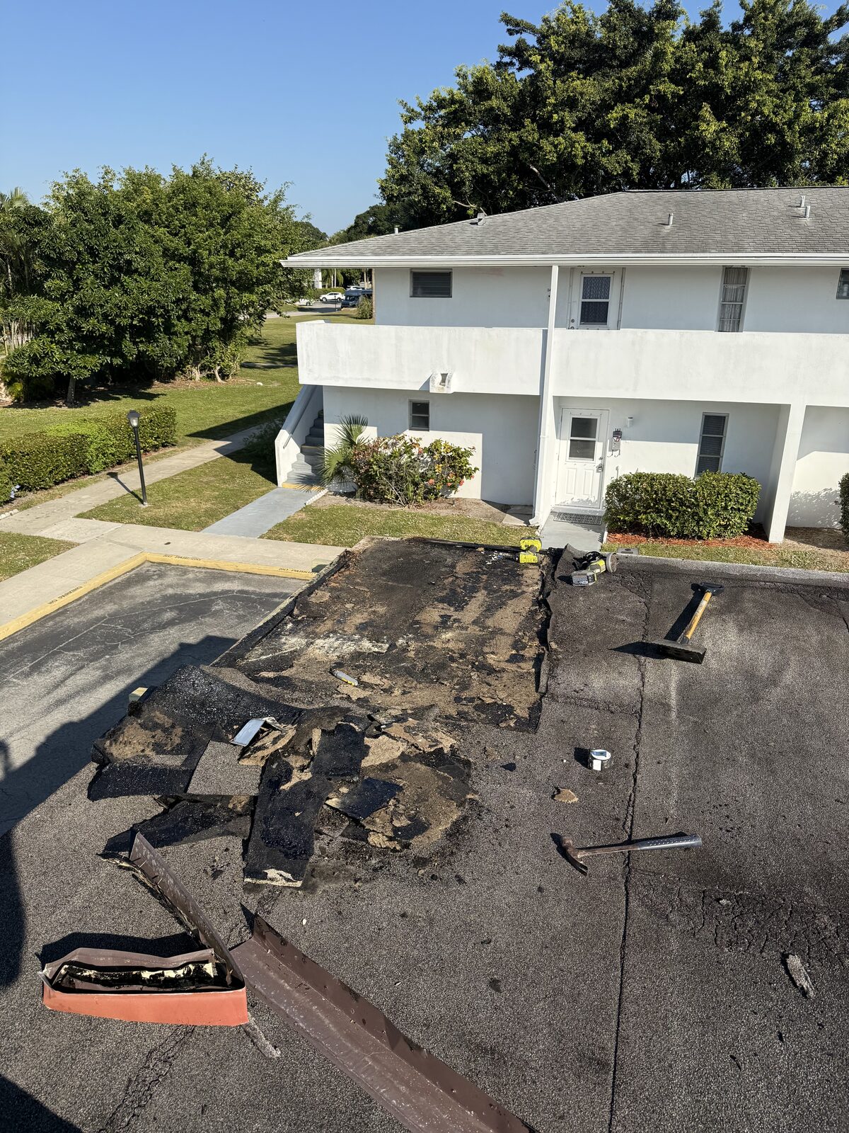 Aged built-up roof membrane torn off a carport deck at Greenway Village, Royal Palm Beach FL, tools laid out on the exposed deck
