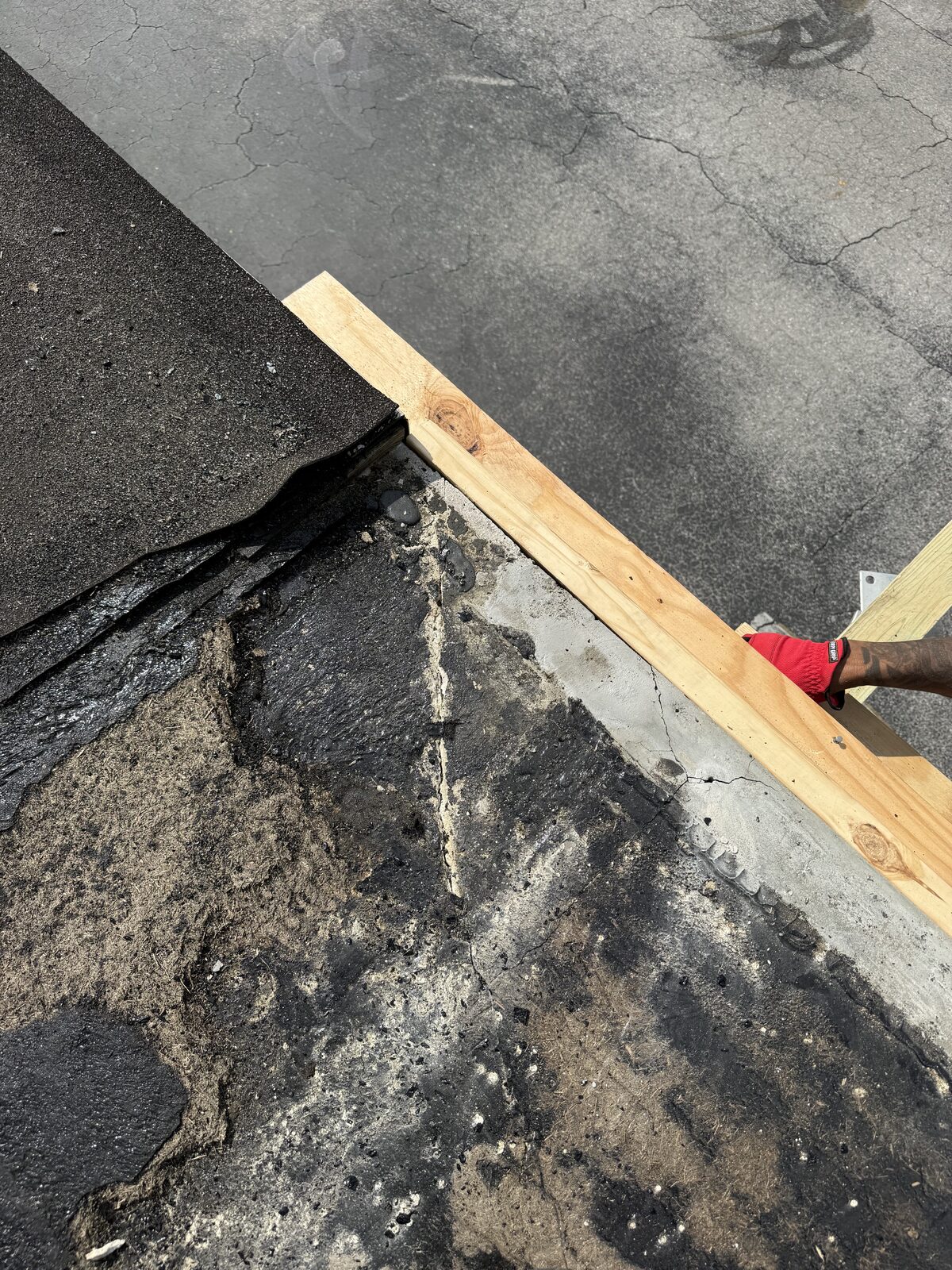 Close-up of the carport roof edge where a new wood nailer is set against the cut-back concrete beam beneath the peeled membrane
