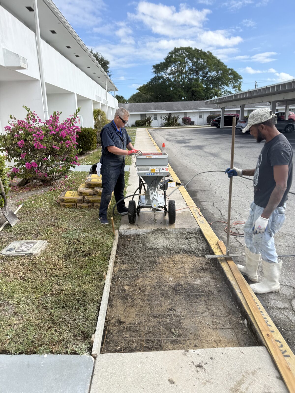 Welded wire mesh laid in the prepared sidewalk bay with timber forms pinned along the curb line, crew working beside the mixer