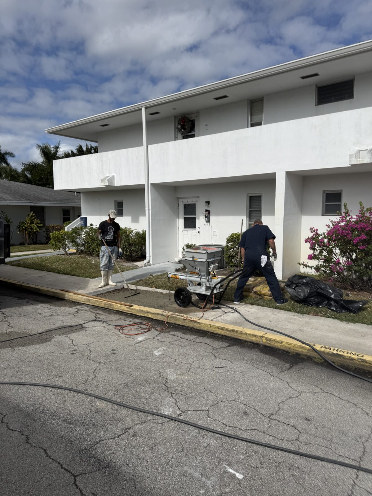 Crew screeding and floating the fresh sidewalk pour level with the adjoining slabs outside a two-storey villa building