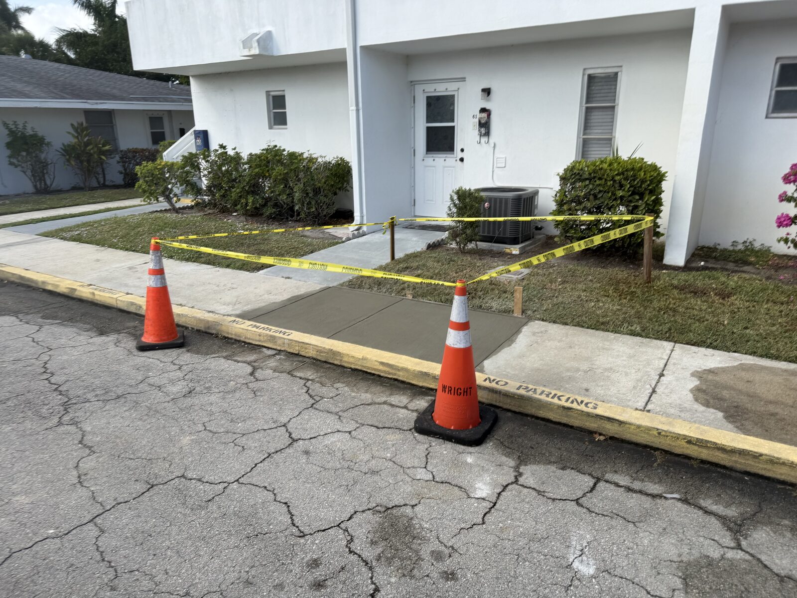 Freshly poured sidewalk panels barricaded with caution tape, stakes and traffic cones outside a resident's front door while the concrete cures