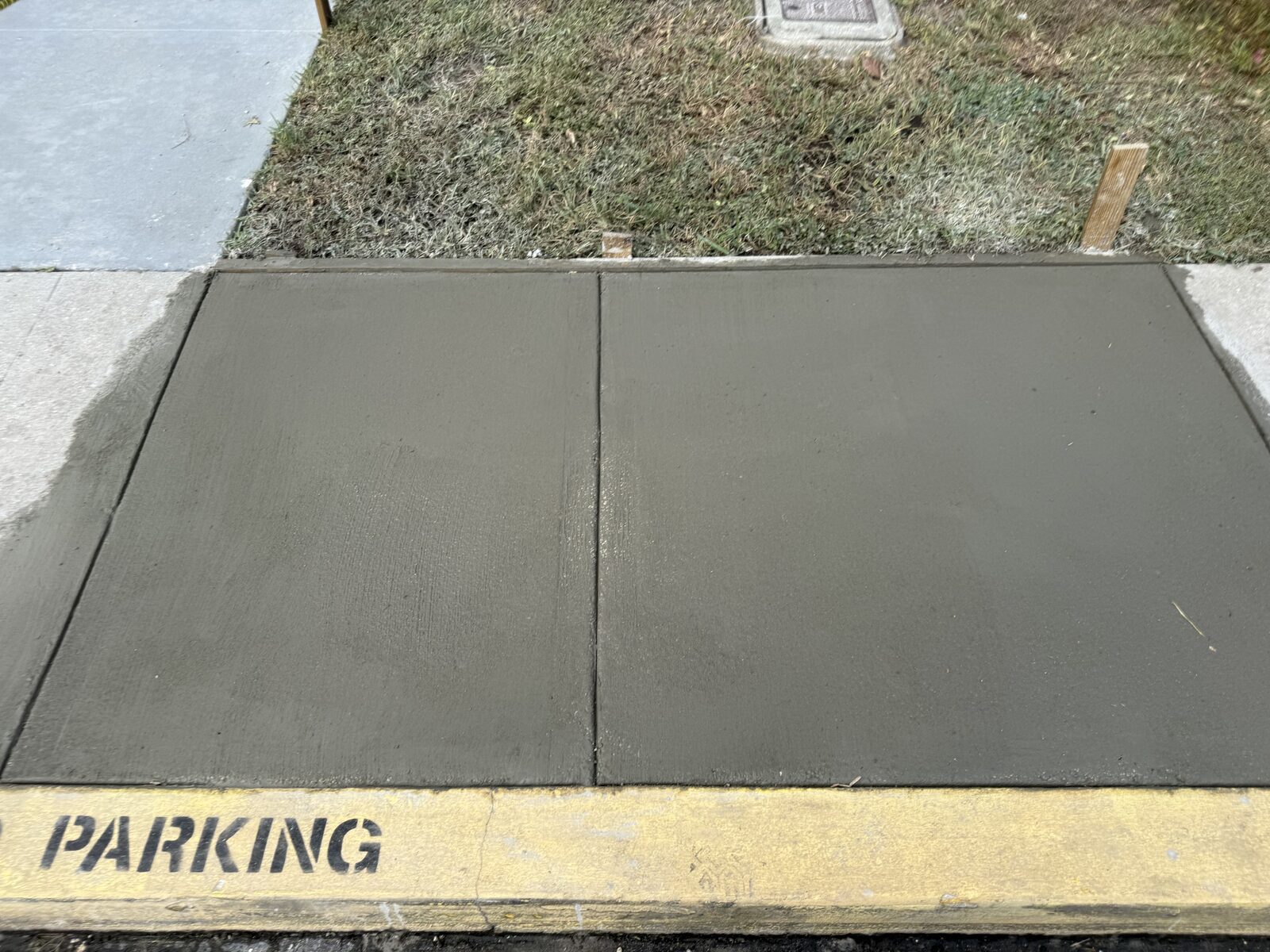 Overhead view of two freshly finished sidewalk panels with a tooled control joint between them, meeting the existing older slab at a clean edge