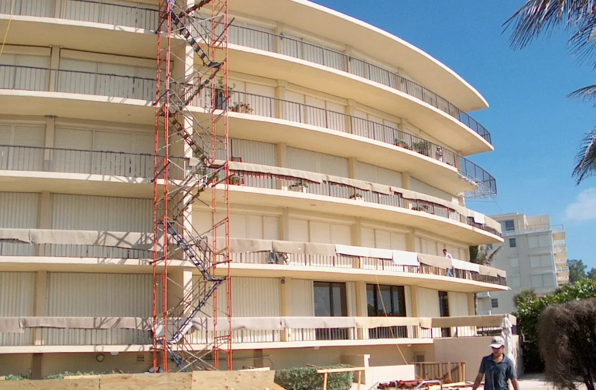 Oceanfront condominium in Palm Beach wrapped in stair-tower scaffolding, with protective sheeting hung along the balcony edges during concrete restoration