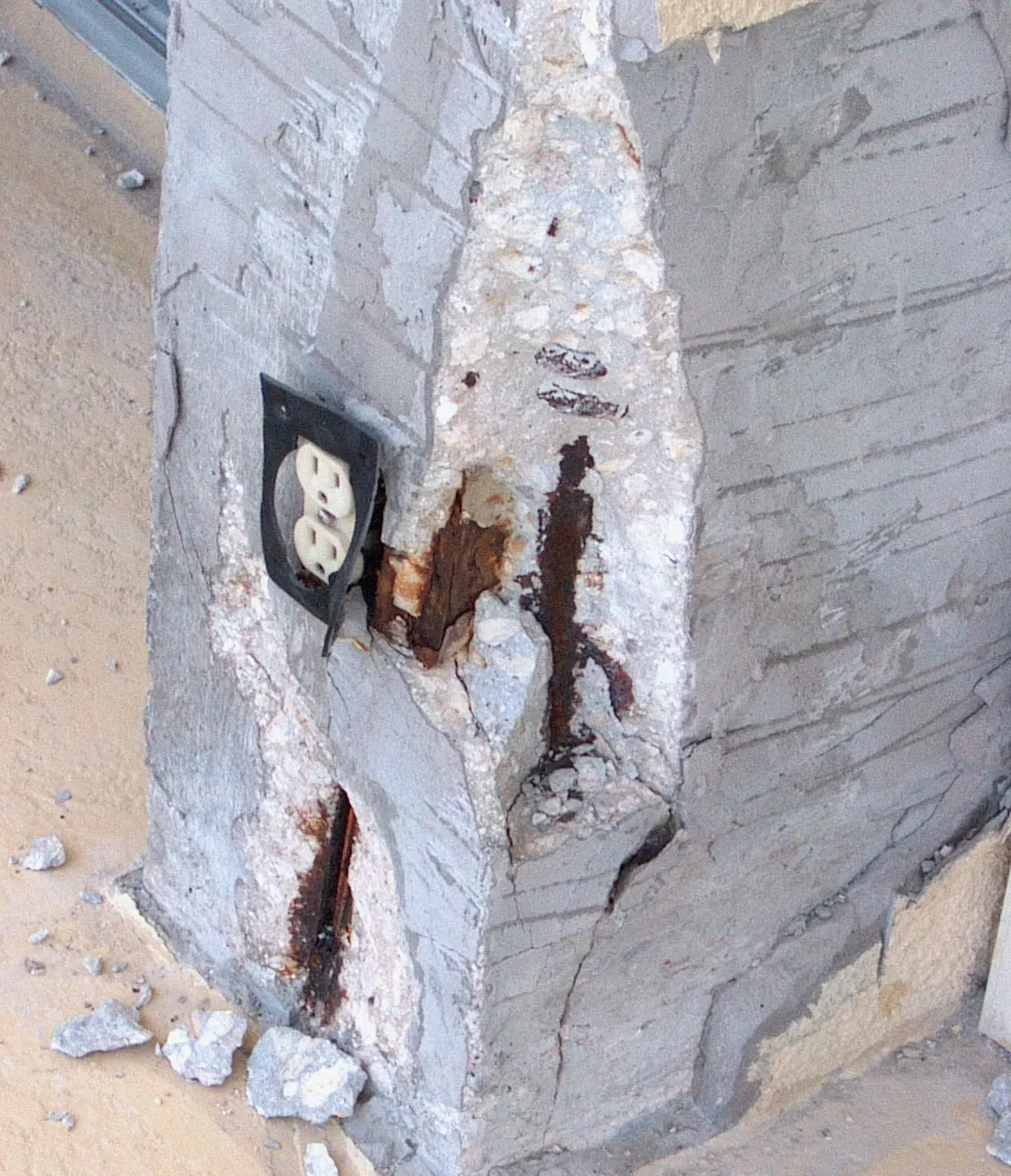 Close-up of a concrete column chipped open around an outlet box, showing heavily corroded reinforcing steel