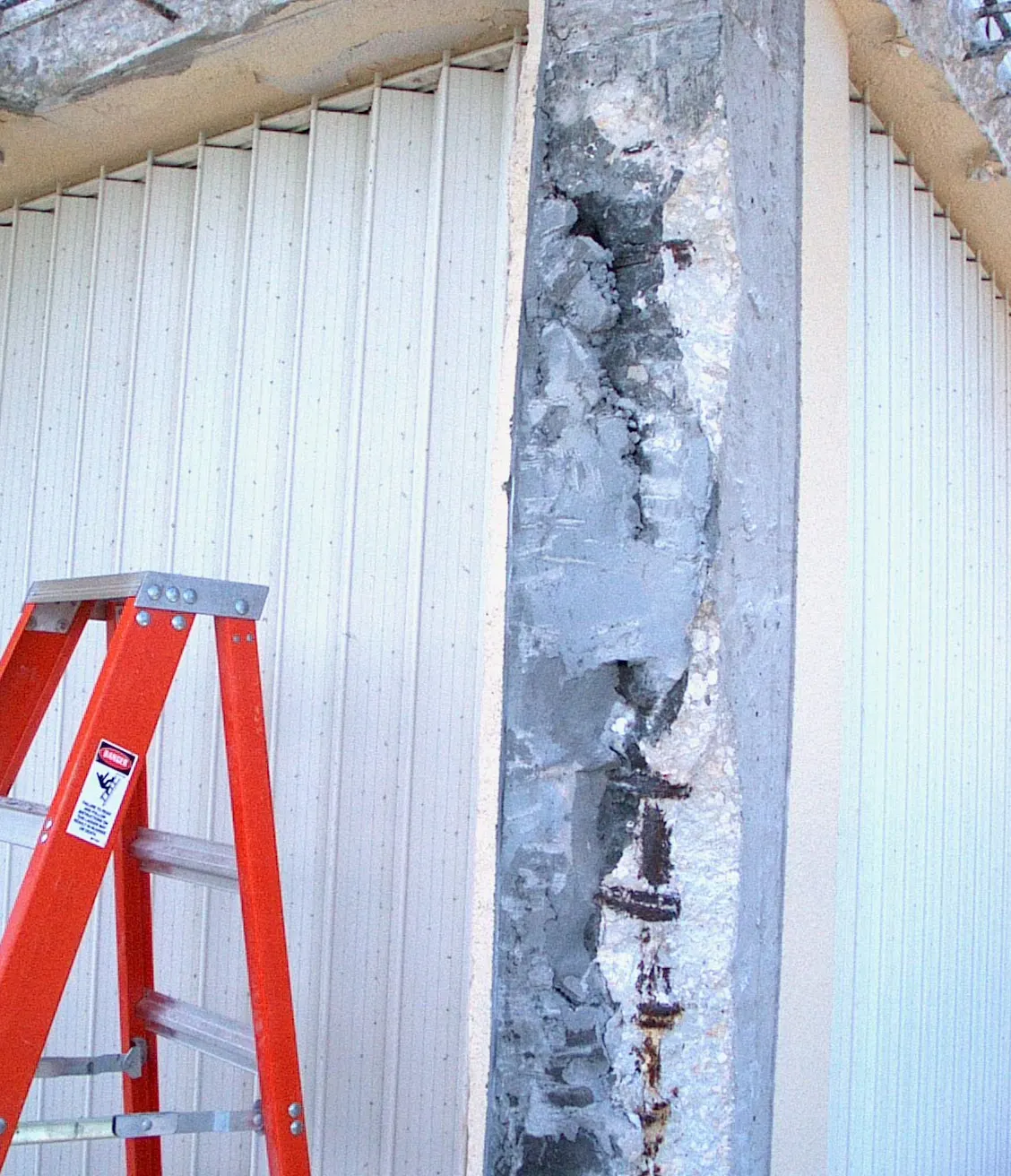 Balcony column chipped back to its reinforcing steel beside a stepladder, ready for cleaning, new steel and patching