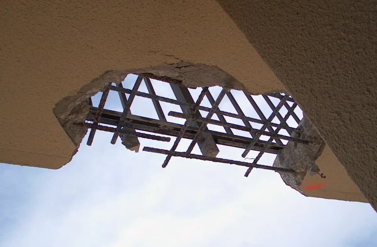 Looking up through an opening cut in a balcony slab, with the reinforcing mesh exposed against the sky