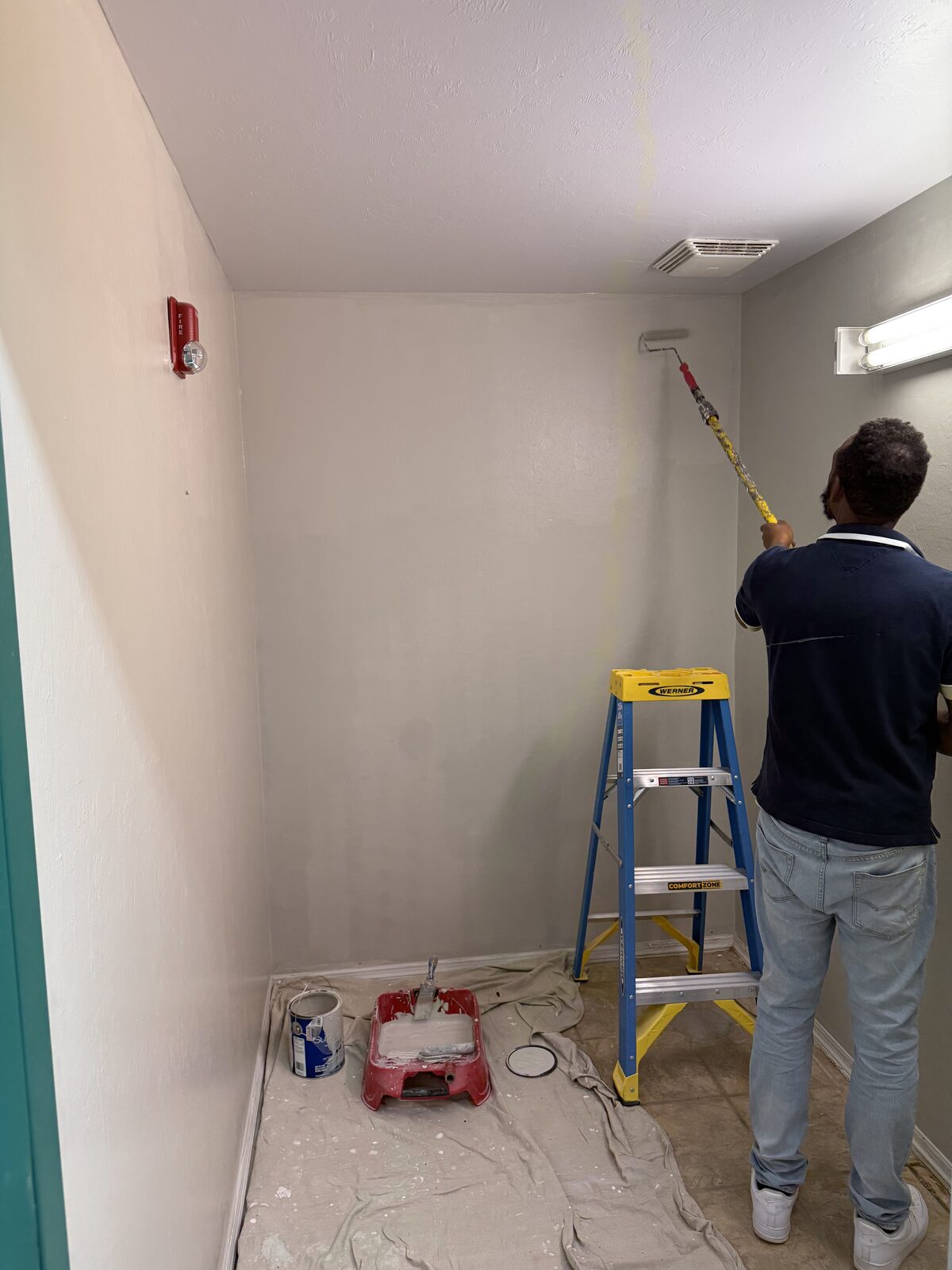 Rolling fresh paint up to the ceiling line on a drop-clothed lobby wall — Bell Engineering & Construction