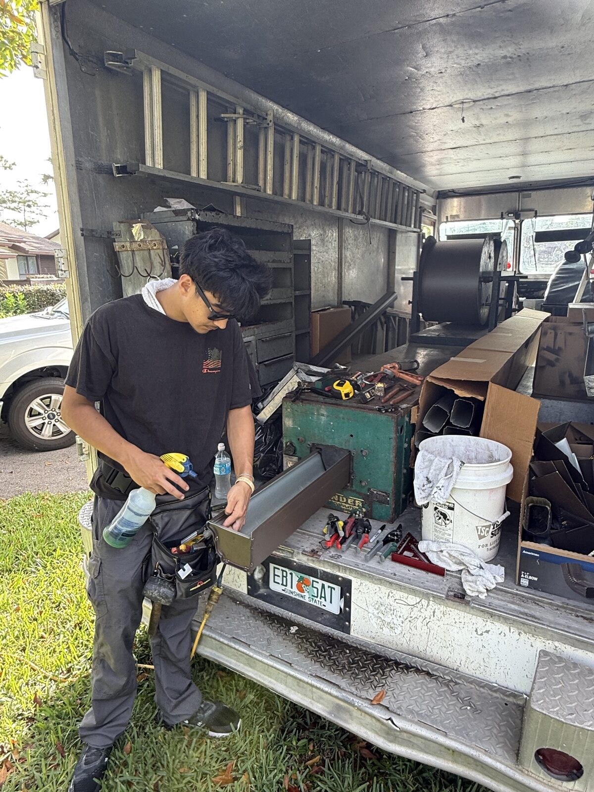 Gutter installer checking a finished brown aluminum downspout outlet section on the tailgate of the gutter van