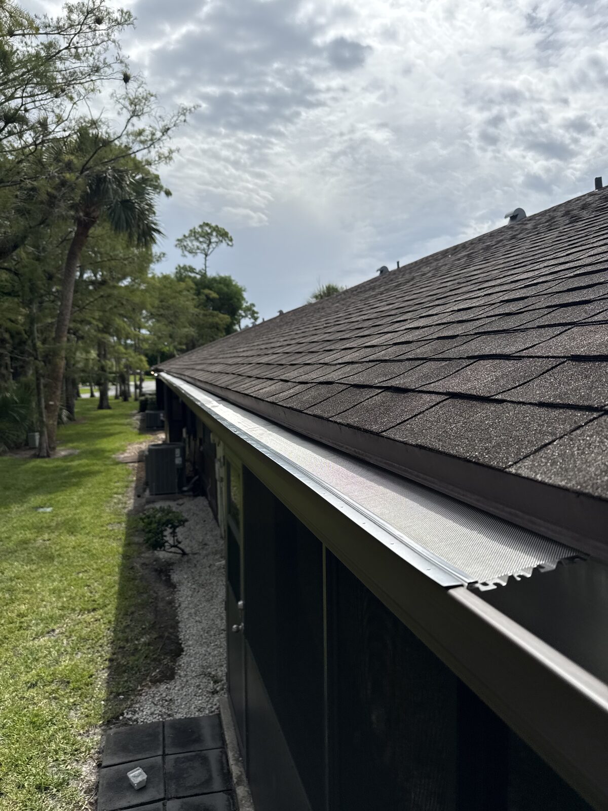 Finished seamless brown gutter with a mesh gutter guard running the full length of a shingle roofline at Strathmore Gate West, Royal Palm Beach