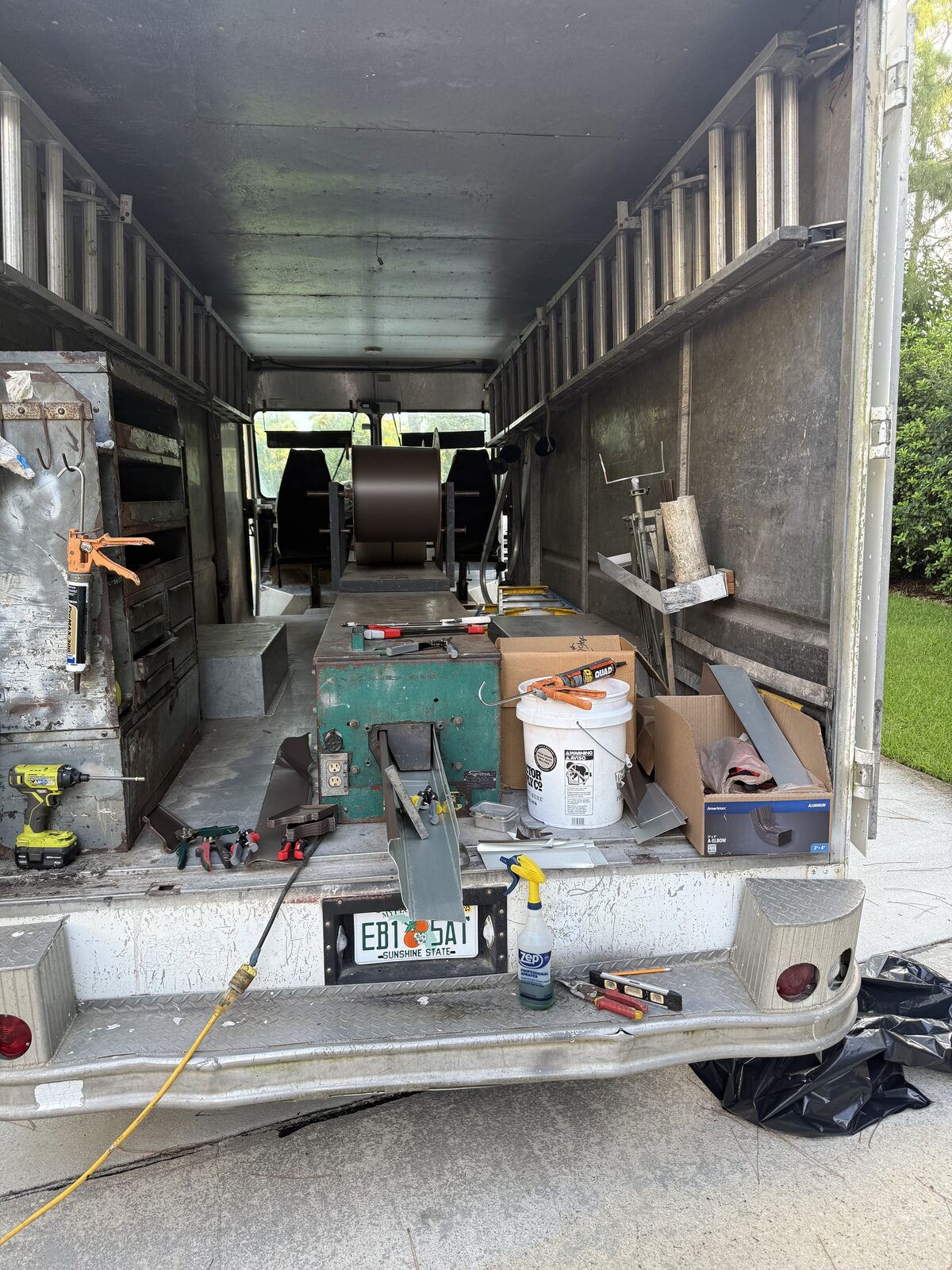 Inside the gutter van: aluminum coil loaded on the reel feeding the roll-forming machine, hand tools, sealant and 3x4 downspout elbows