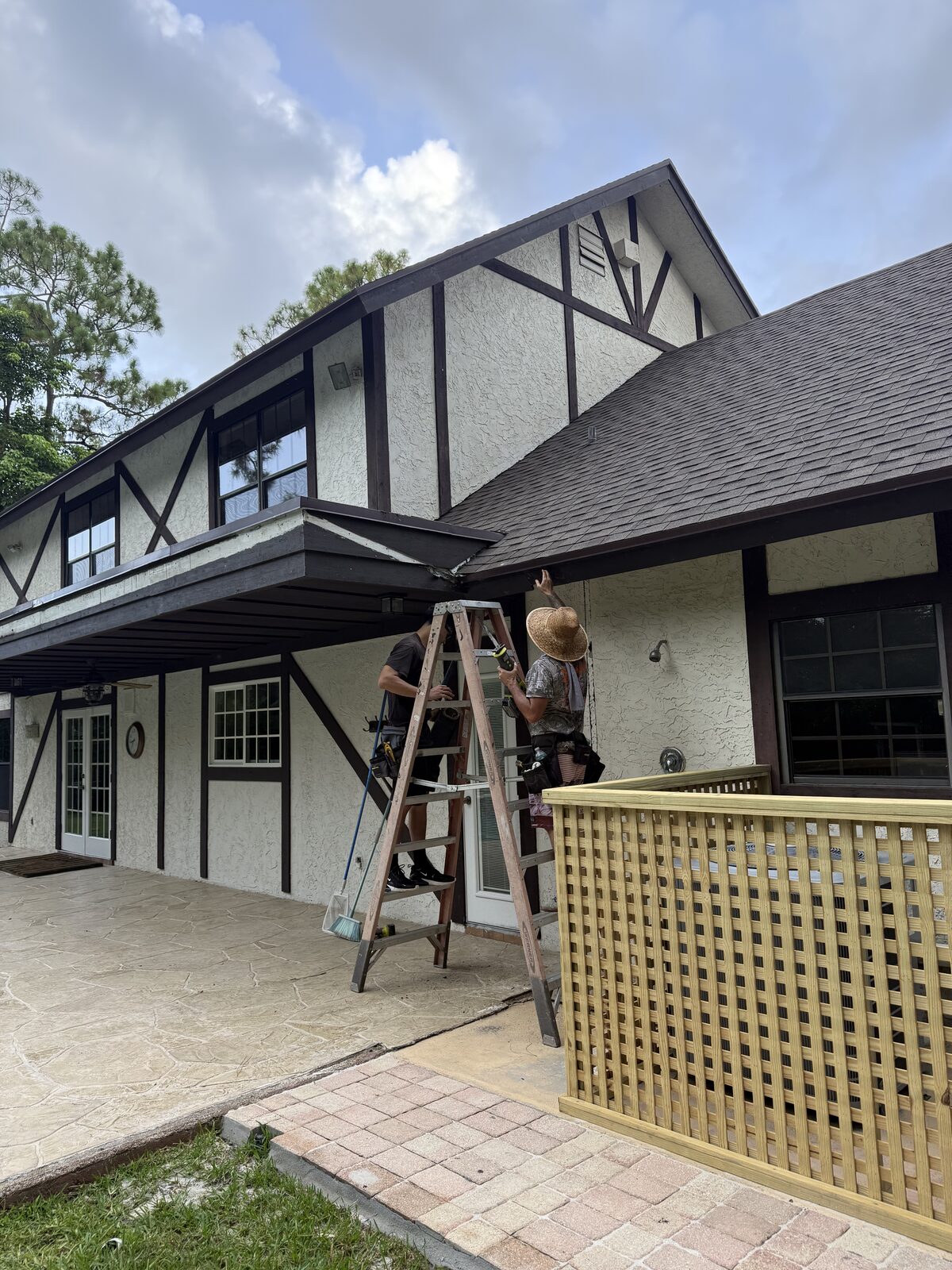 Two crew members on ladders working the eave line of a two-story Tudor-style stucco home in Wellington, Florida during gutter installation