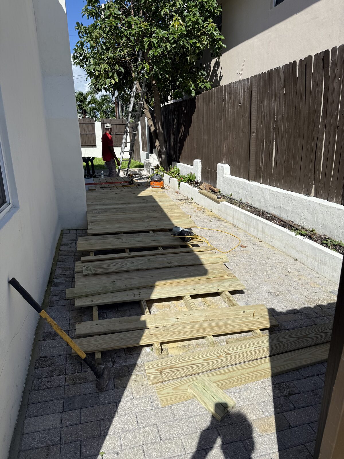 Closely spaced pressure-treated joists running down the length of the side yard with deck boards staged loose across them
