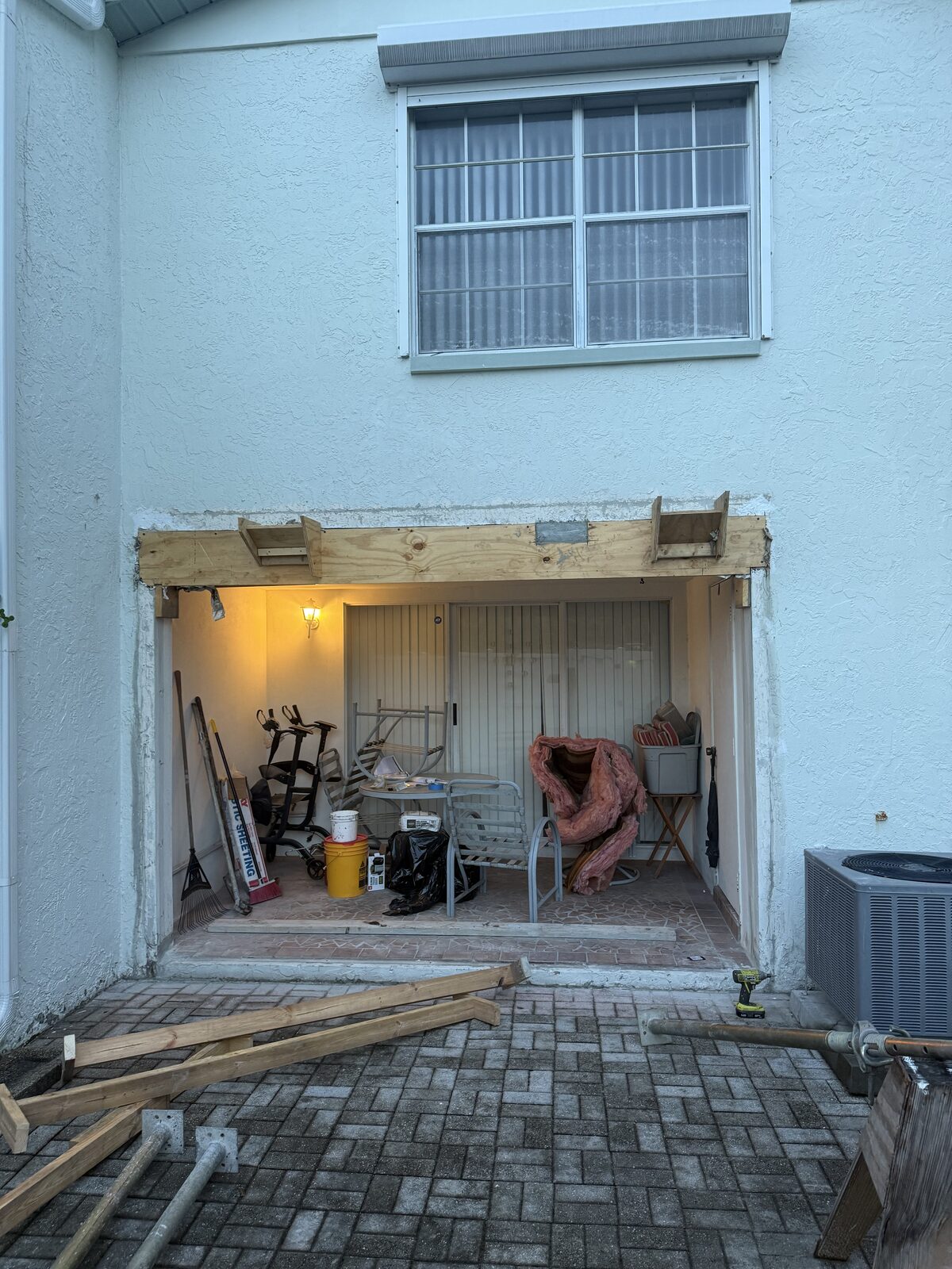Timber formwork built across the patio opening at dusk ready for the beam to be repoured, with shoring posts and lumber stacked on the paver deck
