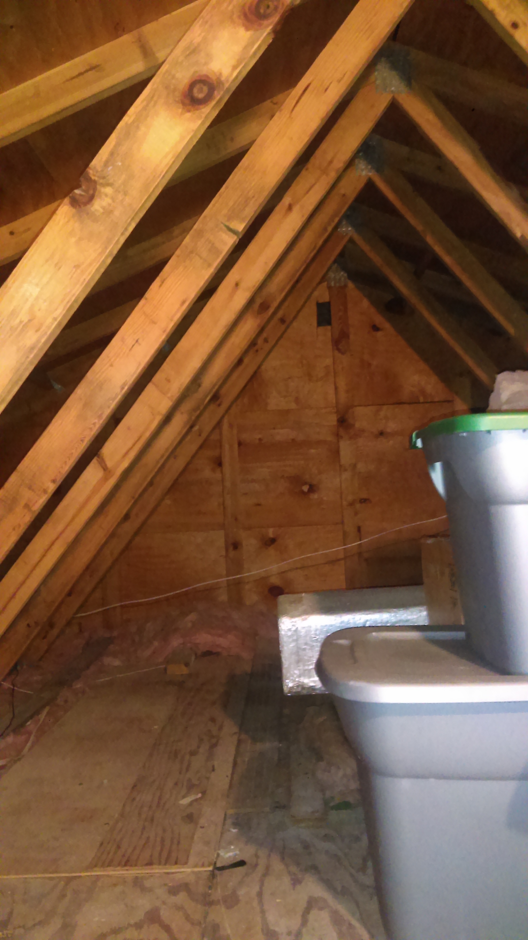 Attic interior showing roof rafters, gable-end sheathing and thin, patchy insulation running out toward the eaves