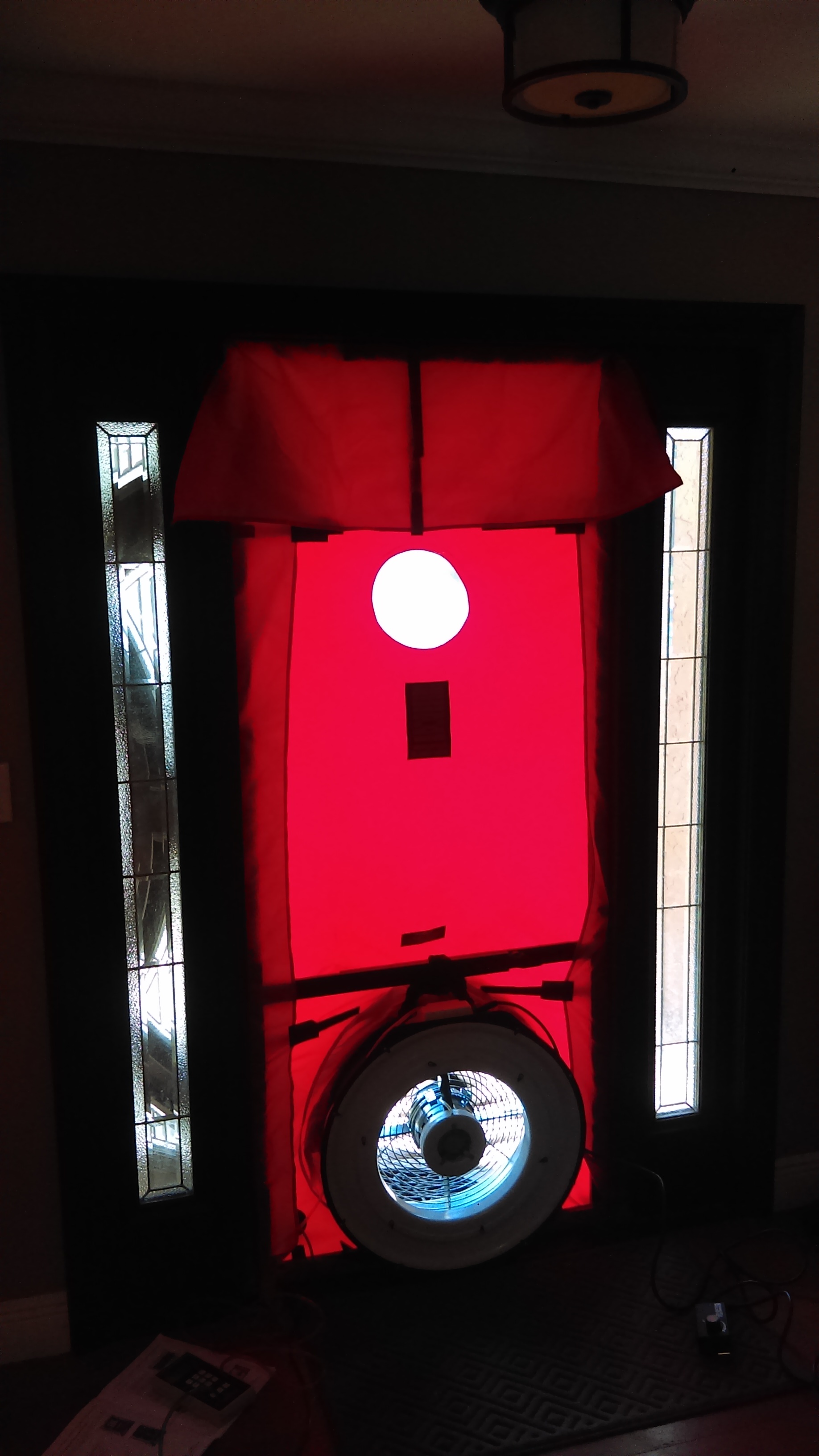 Red blower-door panel and calibrated fan sealed into a residential front entry during an energy audit, with the manometer on the floor