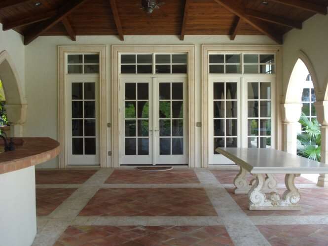 Covered loggia with a beamed wood ceiling, French doors and a carved stone bench on a terracotta tile floor