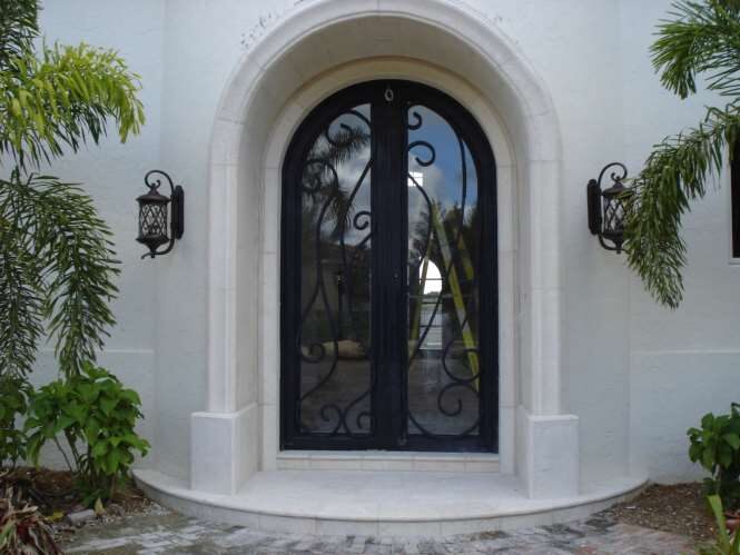 Arched wrought-iron and glass entry door set in a carved stone surround flanked by coach lanterns