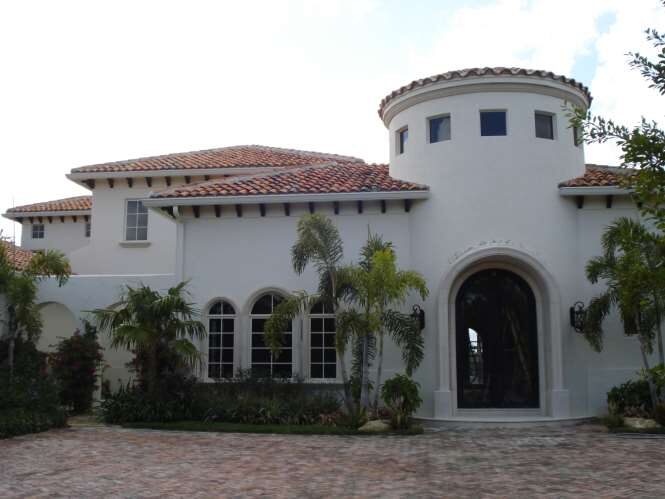 Front elevation of a white stucco Mediterranean estate with a barrel-tile roof, round turret and arched entry