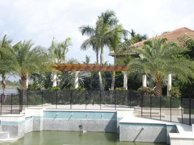 Waterfront pool and spa under construction with a pergola, safety fence and lakefront palms