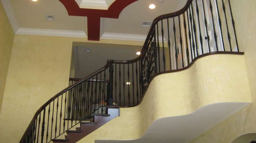 Curved staircase with a dark wood handrail, wrought-iron balusters and a red-inlaid tray ceiling