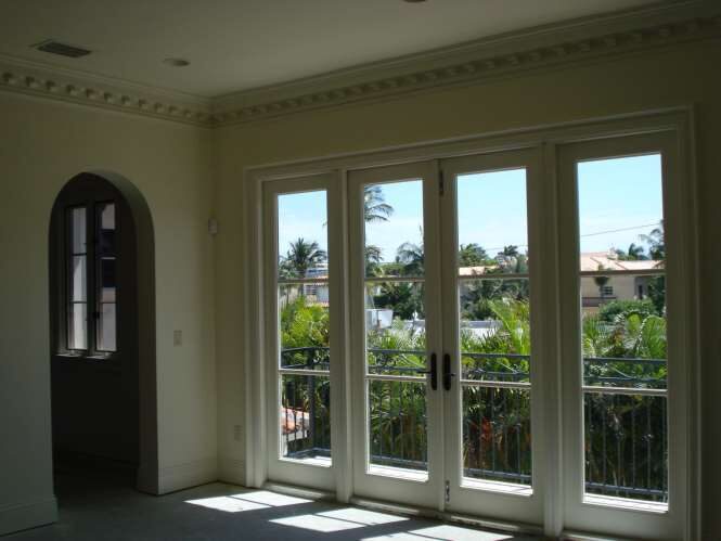 Bright estate room with French doors to a balcony beneath a detailed dentil cornice and arched doorway