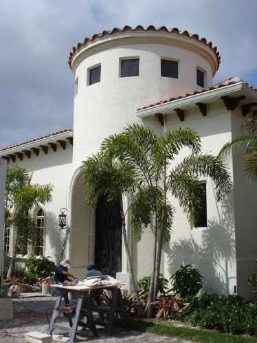 Round stucco turret with a barrel-tile roof under construction, a carpenter at a workbench below