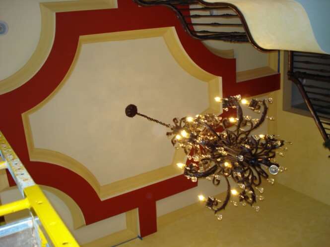 Decorative painted tray ceiling framed in red and gold with an ornate wrought-iron crystal chandelier
