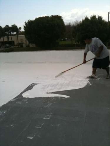 Roofing crew applying a white protective roof coating across a flat commercial roof