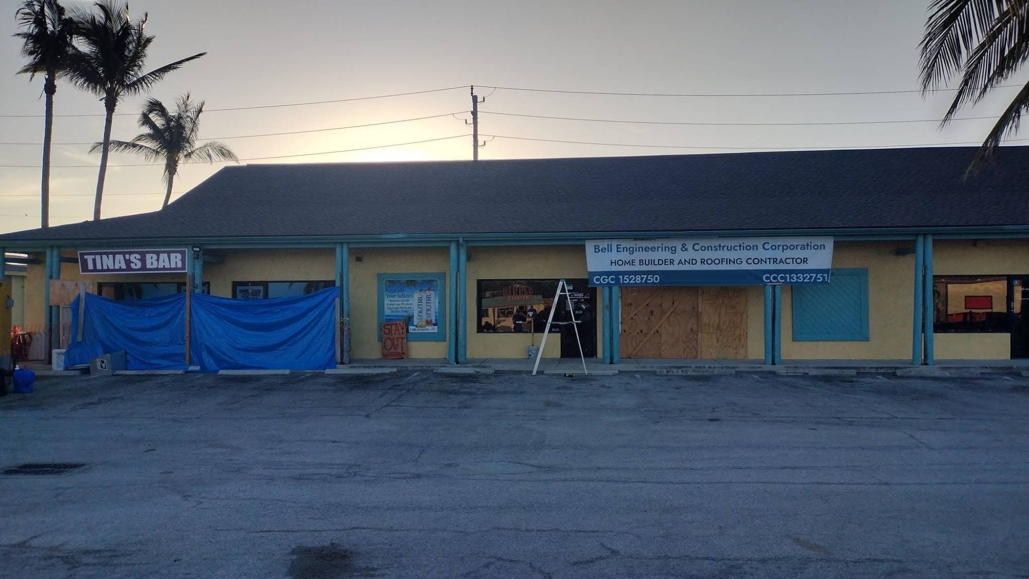 Bell Engineering and Construction Corporation banner hung on a San Carlos Blvd plaza in Fort Myers Beach, storefronts boarded and tarped after Hurricane Ian