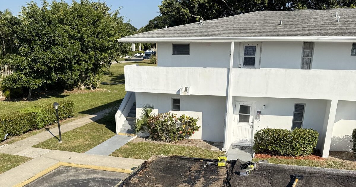 Two-story residential building in a Palm Beach County HOA community with the flat carport roof torn open for repair