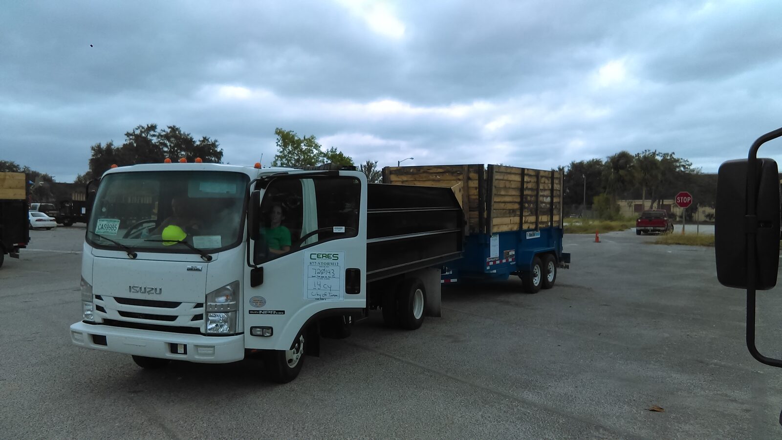 Isuzu NPR-HD dump truck and a loaded dump trailer staged for Hurricane Irma debris hauling in Tampa, a Ceres load ticket taped in the windshield